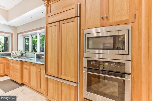 kitchen featuring stone countertops, built in appliances, light brown cabinetry, and light tile patterned floors