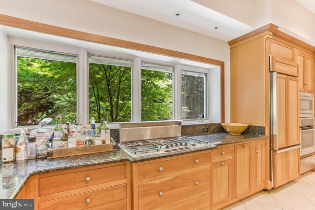 kitchen featuring dark stone countertops, built in appliances, and light tile patterned floors