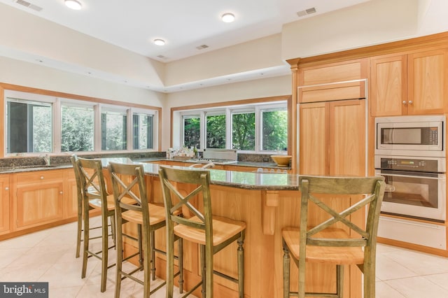 kitchen with visible vents, a kitchen island, built in appliances, light tile patterned floors, and dark stone countertops