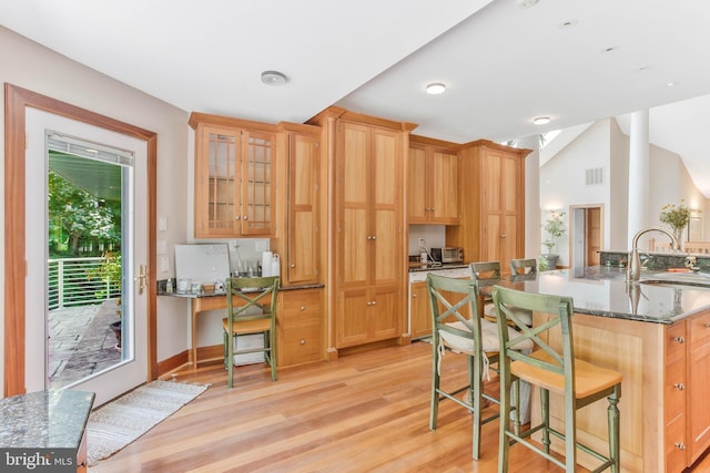 kitchen with glass insert cabinets, a breakfast bar area, dark stone countertops, light wood-style flooring, and a sink