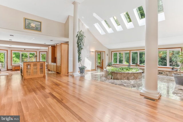 unfurnished living room with baseboards, visible vents, ornate columns, high vaulted ceiling, and light wood-type flooring