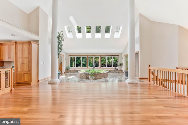 living area featuring decorative columns, light wood finished floors, and high vaulted ceiling