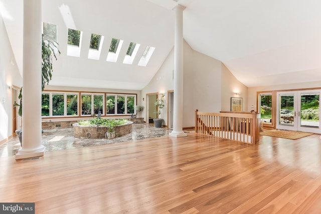 interior space with wood finished floors, ornate columns, high vaulted ceiling, a skylight, and french doors