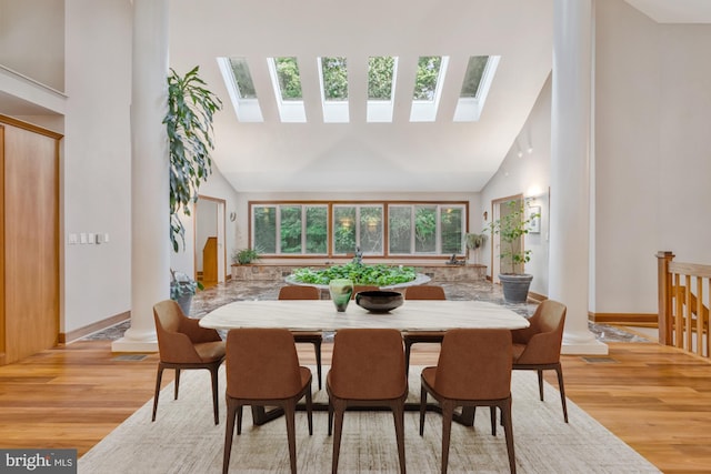 dining room with light wood finished floors, high vaulted ceiling, a skylight, and baseboards