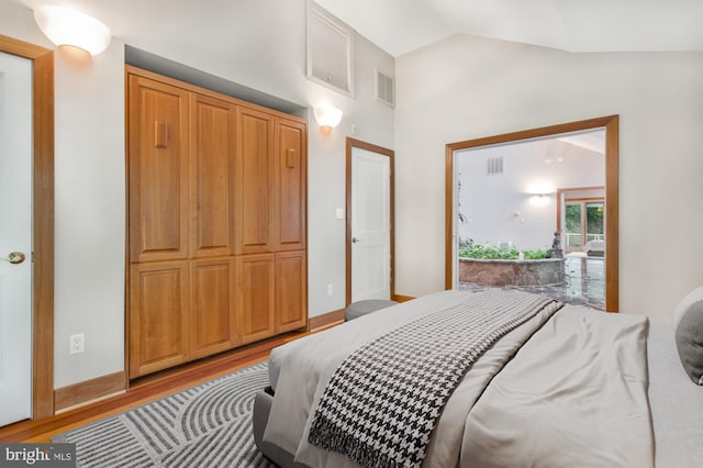 bedroom featuring visible vents, light wood-style flooring, baseboards, and lofted ceiling