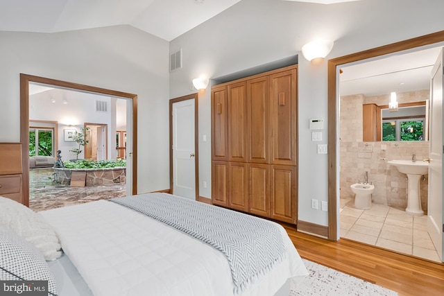 bedroom with vaulted ceiling, visible vents, ensuite bathroom, and wood finished floors