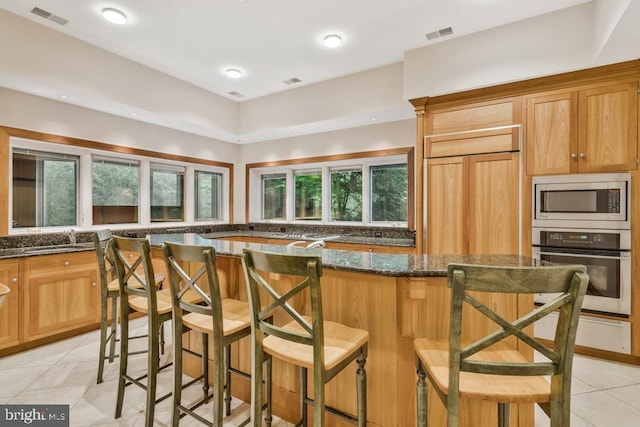 kitchen with visible vents, a kitchen island, built in appliances, a breakfast bar, and dark stone counters