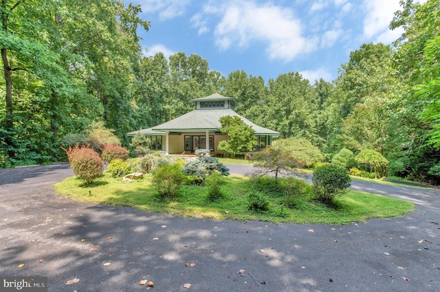 view of front of home featuring aphalt driveway, a porch, and a wooded view