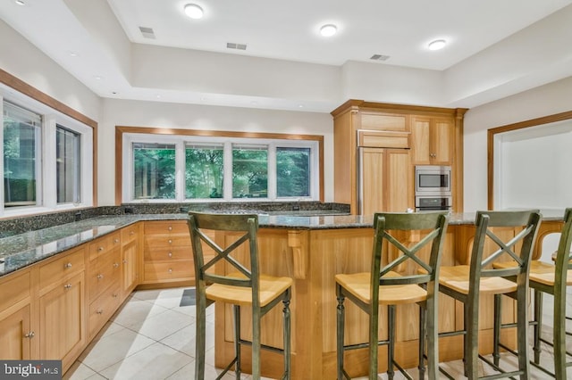 kitchen featuring dark stone counters, a kitchen breakfast bar, visible vents, and built in appliances