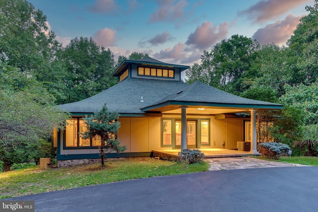 back of property at dusk featuring a shingled roof