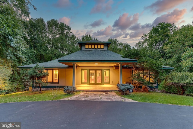 view of front of home with driveway, covered porch, stucco siding, a front lawn, and french doors