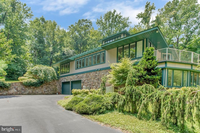 view of front facade with aphalt driveway, an attached garage, stone siding, and stucco siding