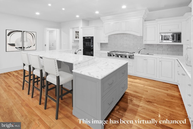 kitchen with white cabinets, light hardwood / wood-style floors, and a kitchen island with sink