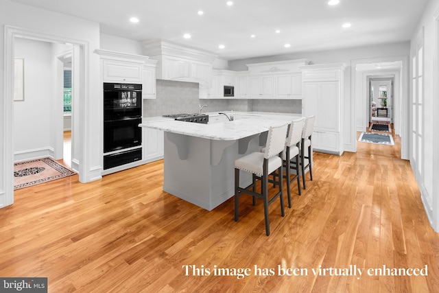 kitchen with double oven, light stone counters, white cabinets, and light wood-type flooring