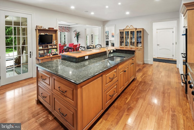 kitchen featuring light hardwood / wood-style floors, a spacious island, sink, and dark stone counters