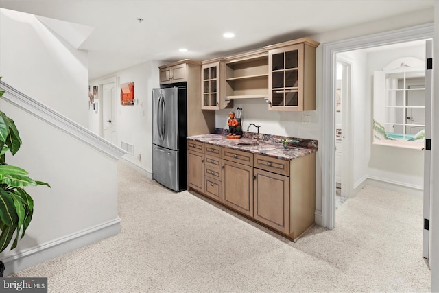 kitchen featuring stone counters, light colored carpet, stainless steel refrigerator, and sink