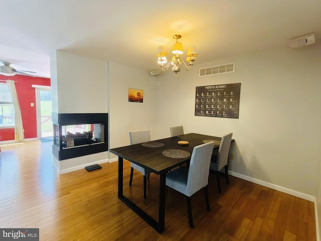 dining area featuring ceiling fan with notable chandelier, a multi sided fireplace, and wood-type flooring