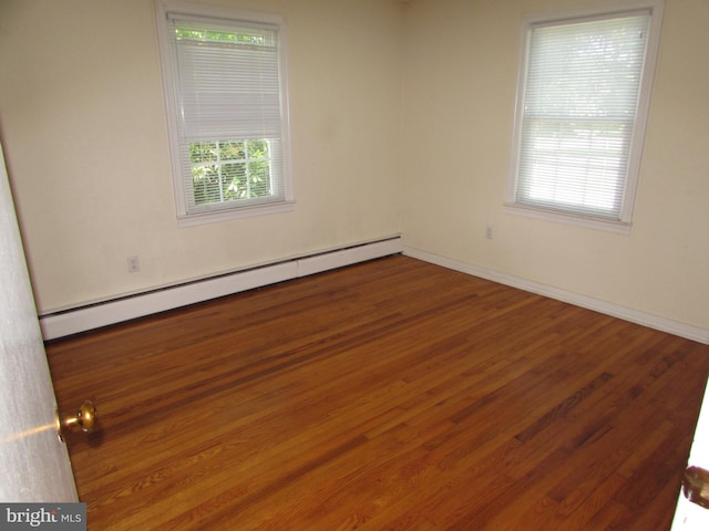 spare room with a wealth of natural light, dark hardwood / wood-style floors, and a baseboard heating unit