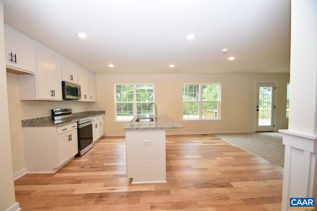 kitchen featuring light stone counters, white cabinetry, stainless steel appliances, and a kitchen island with sink