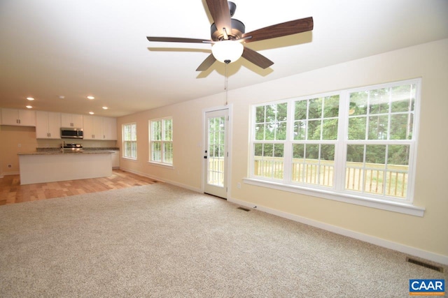 unfurnished living room featuring light carpet and ceiling fan