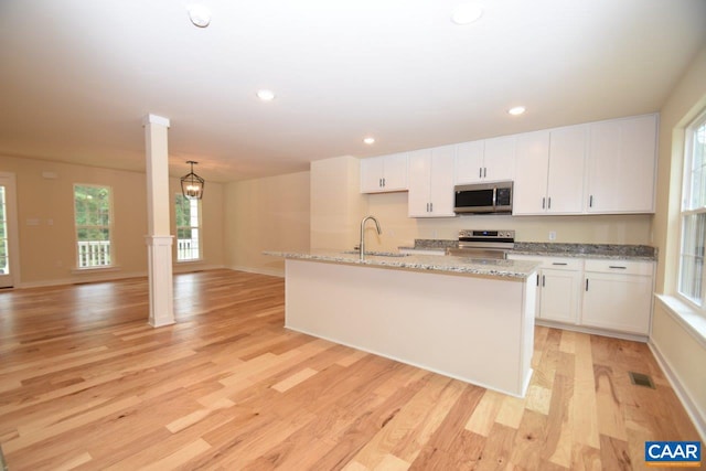 kitchen featuring light wood-type flooring, stainless steel appliances, sink, a center island with sink, and white cabinetry