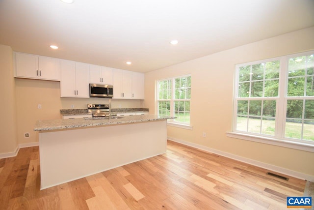 kitchen with white cabinets, stainless steel appliances, light hardwood / wood-style flooring, and a kitchen island with sink