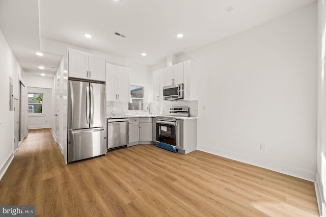 kitchen featuring appliances with stainless steel finishes, light hardwood / wood-style flooring, white cabinetry, and tasteful backsplash