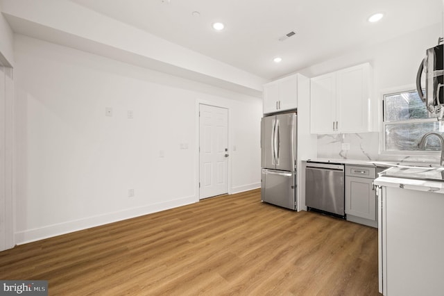 kitchen featuring white cabinetry, sink, stainless steel appliances, decorative backsplash, and light wood-type flooring