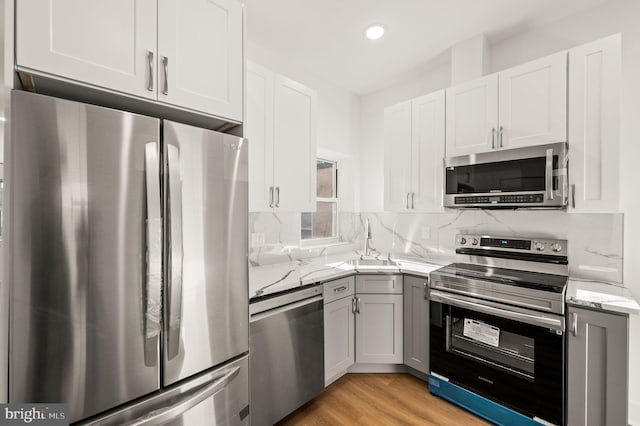 kitchen with white cabinetry, light stone countertops, stainless steel appliances, light hardwood / wood-style flooring, and decorative backsplash