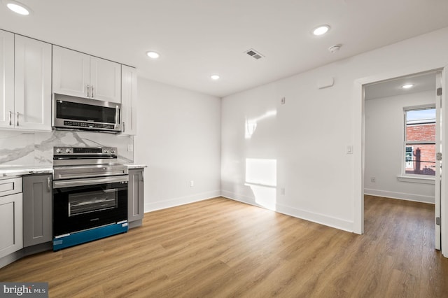 kitchen featuring decorative backsplash, white cabinetry, stainless steel appliances, and light wood-type flooring