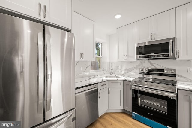 kitchen featuring light stone countertops, appliances with stainless steel finishes, sink, light hardwood / wood-style flooring, and white cabinets