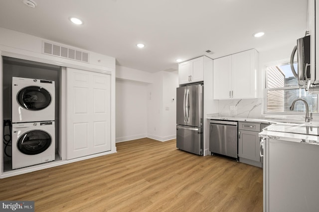 kitchen featuring white cabinetry, tasteful backsplash, stacked washer and dryer, light hardwood / wood-style floors, and appliances with stainless steel finishes