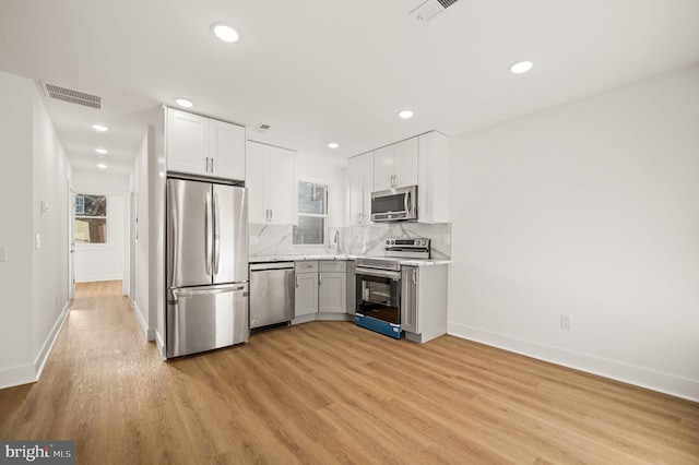 kitchen featuring appliances with stainless steel finishes, backsplash, sink, white cabinets, and light hardwood / wood-style floors