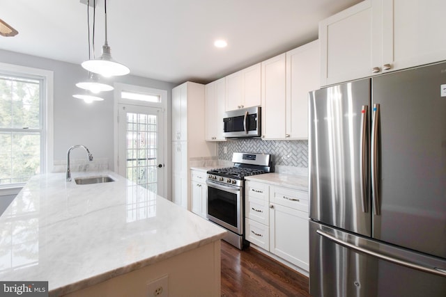 kitchen featuring stainless steel appliances, sink, white cabinetry, hanging light fixtures, and an island with sink