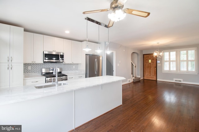 kitchen with dark hardwood / wood-style floors, light stone countertops, appliances with stainless steel finishes, decorative light fixtures, and white cabinetry