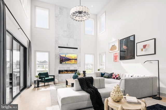 living room featuring light hardwood / wood-style floors, a high end fireplace, a towering ceiling, and a notable chandelier