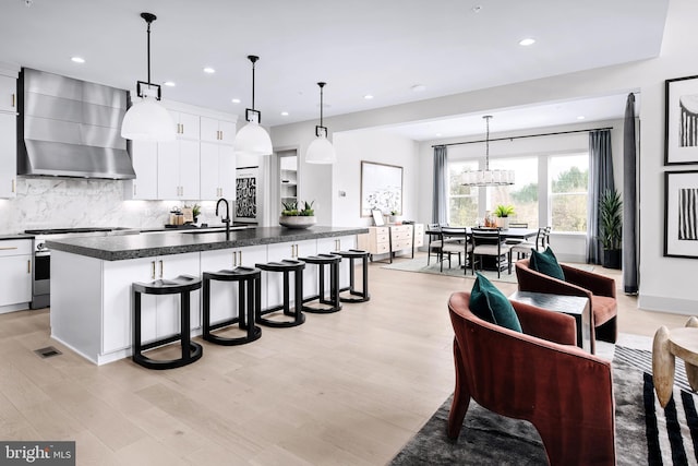 kitchen with white cabinetry, wall chimney range hood, gas stove, and pendant lighting