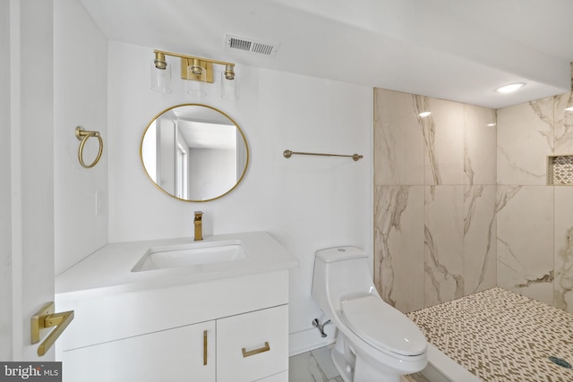 bathroom featuring a tile shower, vanity, and toilet