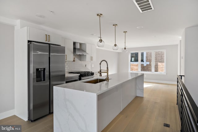 kitchen with white cabinets, a center island with sink, sink, appliances with stainless steel finishes, and decorative light fixtures