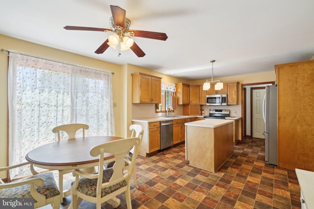 kitchen with ceiling fan, sink, stainless steel appliances, hanging light fixtures, and a kitchen island