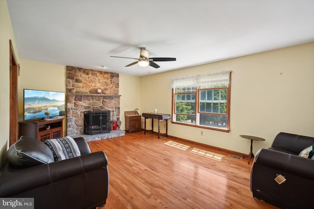 living room featuring light hardwood / wood-style floors, a stone fireplace, and ceiling fan