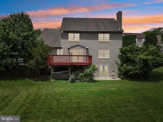 back house at dusk with a deck, a yard, and a patio