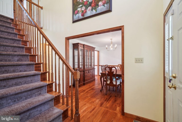 entrance foyer with wood-type flooring, a towering ceiling, and an inviting chandelier