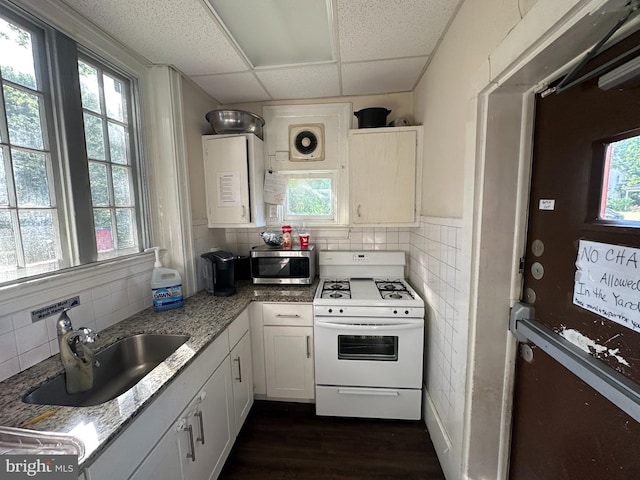 kitchen with a paneled ceiling, white stove, white cabinets, sink, and light stone counters