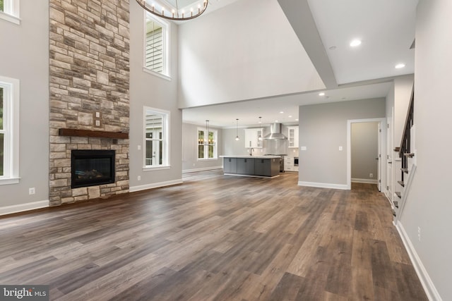 unfurnished living room featuring a fireplace, a towering ceiling, dark hardwood / wood-style floors, and an inviting chandelier