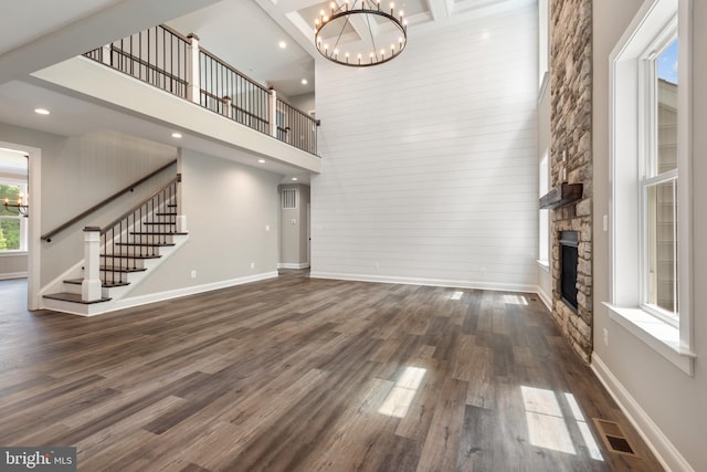 unfurnished living room with a high ceiling, a stone fireplace, dark wood-type flooring, and a notable chandelier