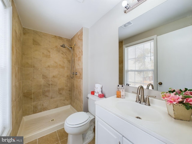 bathroom with toilet, vanity, tile patterned flooring, and a tile shower