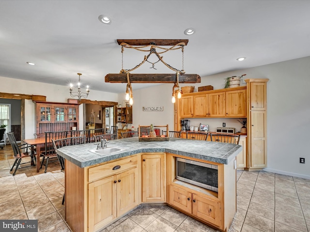 kitchen featuring light brown cabinetry, a center island with sink, hanging light fixtures, and sink