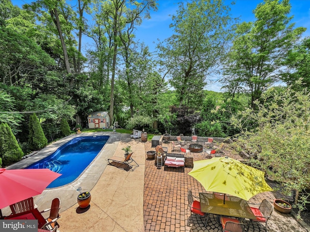 view of pool featuring a patio, a fire pit, and a storage shed