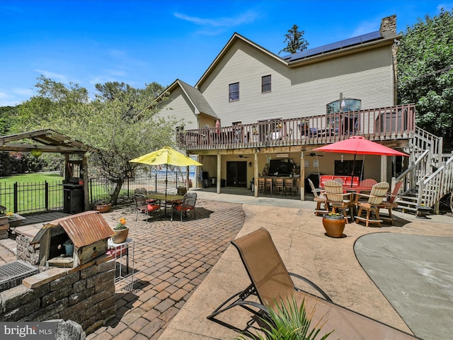 back of house featuring a patio, exterior bar, a deck, and solar panels